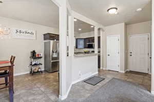 Kitchen with light tile patterned floors, stainless steel appliances, arched walkways, dark brown cabinets, and a textured ceiling