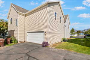 View of side of property with a lawn, an attached garage, a mountain view, driveway, and roof with shingles