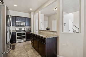 Kitchen featuring stainless steel appliances, light stone counters, light tile patterned floors, a textured ceiling, and recessed lighting