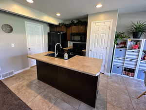 Kitchen featuring dark brown cabinetry, a textured ceiling, light countertops, recessed lighting, and an island with sink