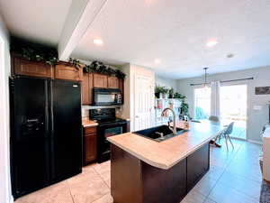 Kitchen featuring black appliances, decorative light fixtures, light countertops, an island with sink, and recessed lighting