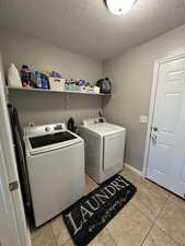 Washroom with a textured ceiling, light tile patterned floors, and washer and dryer