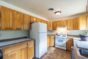 Kitchen with white appliances, stone finish flooring, under cabinet range hood, and brown cabinets