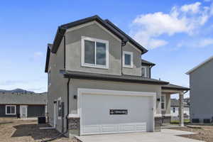 View of front facade featuring stucco siding, a garage, concrete driveway, and stone siding
