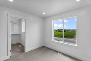Unfurnished bedroom with light carpet, a walk in closet, and recessed lighting
