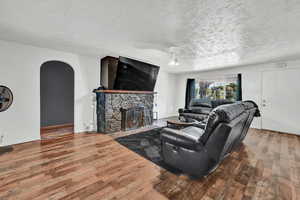 Living room featuring arched walkways, wood finished floors, a stone fireplace, a textured ceiling, and ceiling fan