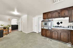Kitchen with arched walkways, light countertops, stainless steel oven, dark brown cabinets, and under cabinet range hood