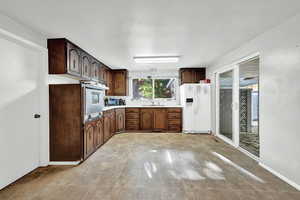 Kitchen with white fridge with ice dispenser, light countertops, dark brown cabinets, wall oven, and stainless steel microwave