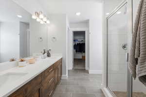 Bathroom with a walk in closet, double vanity, a stall shower, light tile patterned flooring, and recessed lighting