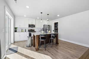 Kitchen with white cabinets, decorative light fixtures, a kitchen breakfast bar, light wood-style floors, and recessed lighting