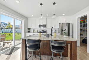 Kitchen with appliances with stainless steel finishes, light wood-type flooring, light stone counters, an island with sink, and white cabinets