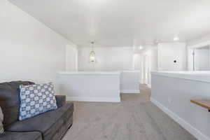 Living area with light colored carpet and an upstairs landing