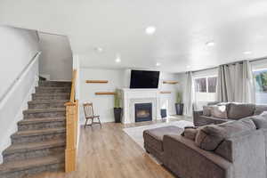 Living room with stairway, light wood finished floors, a lit fireplace, and recessed lighting