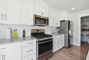 Kitchen featuring stainless steel appliances, white cabinets, light stone counters, light wood finished floors, and decorative backsplash