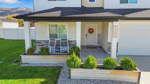 Doorway to property with covered porch, a shingled roof, stone siding, and a garage