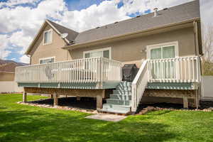 Rear view of house featuring stucco siding, a yard, a wooden deck, and roof with shingles