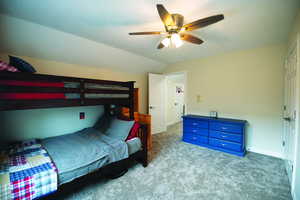 Carpeted bedroom featuring vaulted ceiling and ceiling fan