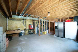 Unfinished basement featuring stainless steel fridge with ice dispenser, freestanding refrigerator, and a water softener system