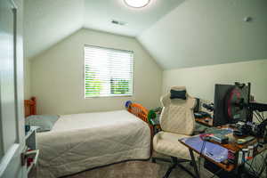 Bedroom with a textured ceiling, vaulted ceiling, and carpet flooring