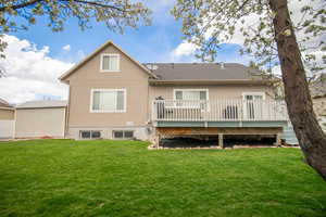 Rear view of house with stucco siding, a wooden deck, a yard, and a shingled roof