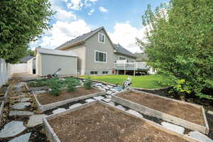 Rear view of property with stucco siding, a lawn, a vegetable garden, a deck, and an outdoor structure
