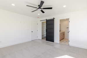 Unfurnished bedroom featuring a barn door, recessed lighting, light carpet, a walk in closet, and ensuite bathroom