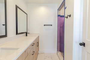 Full bathroom with light marble finish flooring, a shower with shower curtain, and double vanity