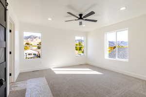 Empty room with light carpet, recessed lighting, a barn door, a mountain view, and a ceiling fan