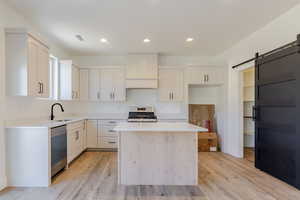 Kitchen with a barn door, light wood-type flooring, a kitchen island, recessed lighting, and appliances with stainless steel finishes