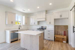 Kitchen with stainless steel appliances, light wood-style floors, a kitchen island, recessed lighting, and white cabinetry