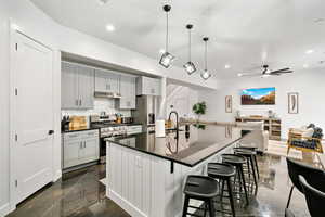 Kitchen with backsplash, stainless steel appliances, open floor plan, a kitchen bar, and ceiling fan