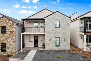 View of front of home with stone siding, stucco siding, and a balcony