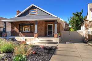 View of front of property featuring a gate, a porch, a shingled roof, a chimney, and brick siding