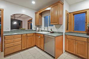 Kitchen featuring stainless steel dishwasher, light tile patterned flooring, brown cabinetry, and arched walkways
