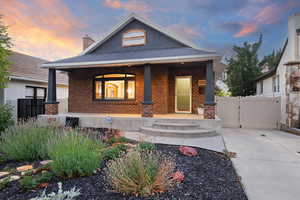 View of front of home with brick siding, covered porch, a gate, a chimney, and a shingled roof