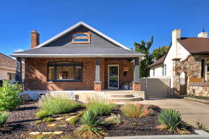 View of front of house with a gate, a porch, roof with shingles, a chimney, and brick siding