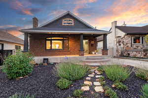 View of front of house featuring a porch, a chimney, and brick siding