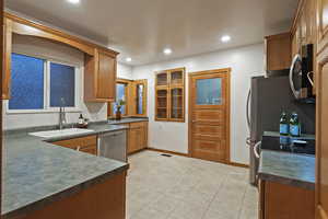 Kitchen featuring brown cabinetry, appliances with stainless steel finishes, dark countertops, recessed lighting, and light tile patterned floors