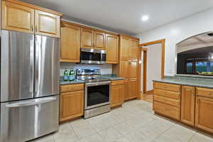 Kitchen featuring appliances with stainless steel finishes, light tile patterned floors, dark countertops, brown cabinetry, and recessed lighting