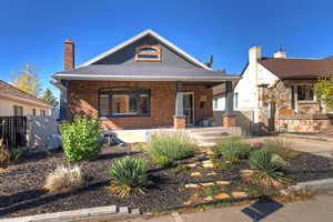 Bungalow-style home with covered porch, a chimney, brick siding, and roof with shingles