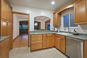 Kitchen featuring dishwasher, brown cabinets, light tile patterned floors, dark countertops, and arched walkways