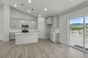 Kitchen with decorative backsplash, lofted ceiling, decorative light fixtures, a kitchen island with sink, and light wood-style floors