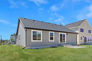 Rear view of house featuring a lawn, a shingled roof, entry steps, and stucco siding