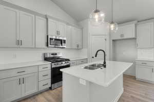 Kitchen featuring tasteful backsplash, appliances with stainless steel finishes, vaulted ceiling, a kitchen island with sink, and light wood-style floors