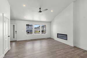 Unfurnished living room with a glass covered fireplace, wood finished floors, ceiling fan, recessed lighting, and lofted ceiling