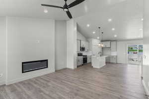 Kitchen with open floor plan, stainless steel appliances, a kitchen island with sink, vaulted ceiling, and light wood finished floors