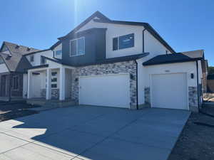 View of front of house with stone siding, a garage, concrete driveway, and stucco siding