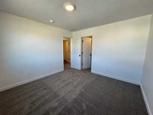 Empty room with dark colored carpet and a textured ceiling