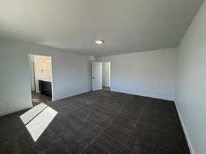 Unfurnished bedroom featuring dark carpet, connected bathroom, and a textured ceiling