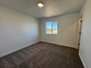 Empty room featuring dark colored carpet and a textured ceiling